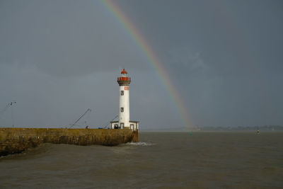 Lighthouse by sea against rainbow in sky