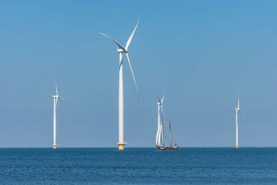 Wind turbines in sea against clear sky