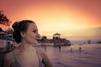 Close-up of thoughtful woman standing at beach against sky during sunset