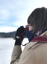 Side view of young woman photographing on field during winter