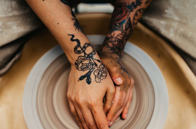 Closeup of dirty hands of anonymous craftsman using pottery wheel and making clay pot in workshop