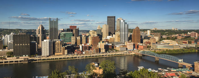 Bridge over river amidst buildings in city against sky