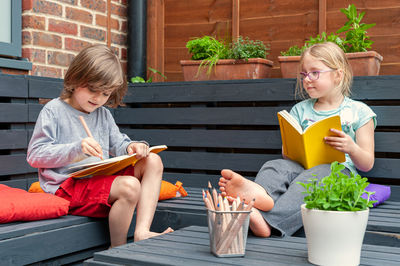 Two little friends from school sitting together in garden and doing homework.