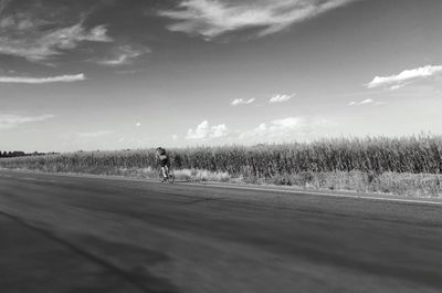 Man cycling on road against sky