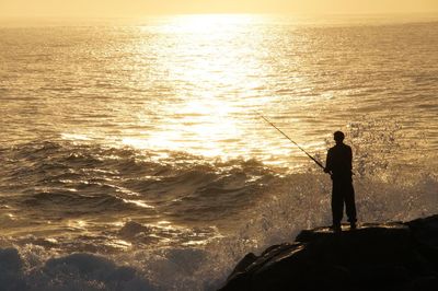 Silhouette man fishing in sea against sunset sky