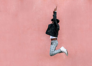 Rear view of woman with arms raised against wall