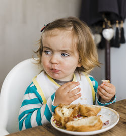 Cute girl eating bread at table in home