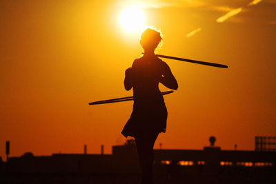 Silhouette of woman twirling hula hoops at sunset