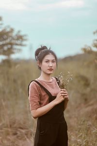 Portrait of woman holding plants while standing on field