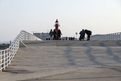 People on walkway by lighthouse against clear sky