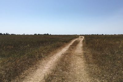 Dirt road amidst field against clear sky