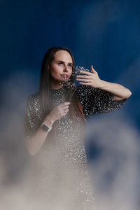 A girl in a dress with polka dots holds a white gypsophila in her hands against a blue wall