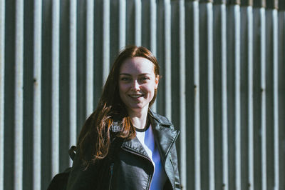 Portrait of smiling young woman standing against wall