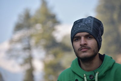 Portrait of young man wearing knit hat against trees