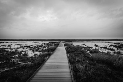 Boardwalk leading towards sea against sky