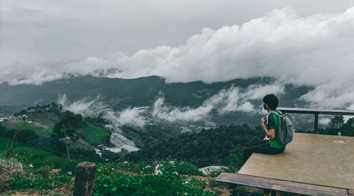 Man sitting on mountain against sky