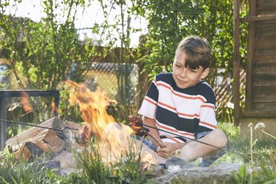 Boy preparing food in bonfire against plants