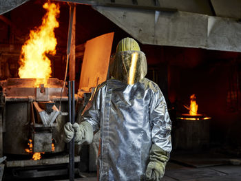 Foundry worker wearing protective helmet with face shield standing in burning factory