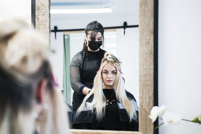 Hairdresser doing hairstyle of customer in front of mirror at salon