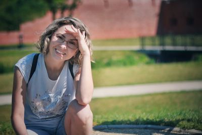 Portrait of smiling woman shielding eyes while sitting outdoors