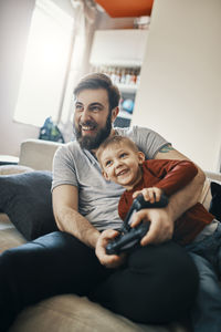 Laughing father and little son sitting together on the couch playing computer game