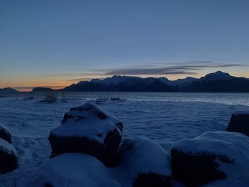 Scenic view of sea by snowcapped mountains against sky during sunset