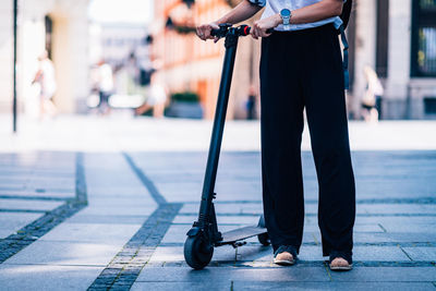 Low section of woman with push scooter standing on footpath