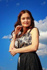 Portrait of smiling woman standing against blue sky