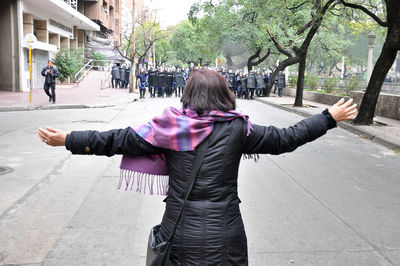 Rear view of woman with arms outstretched walking on street in city