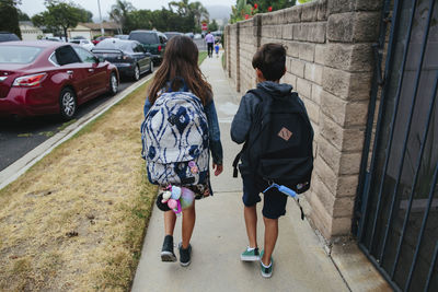 Rear view of siblings with backpack walking on footpath