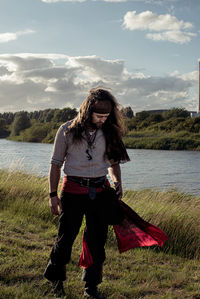 Full length of young woman standing by lake against sky