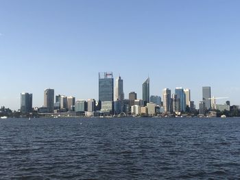 Sea by modern buildings against clear sky