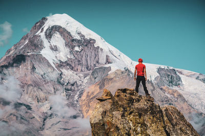 Rear view of young man standing on rock formation against mountain and sky