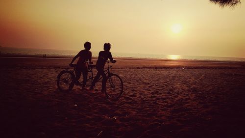 People riding bicycle at beach against sky during sunset