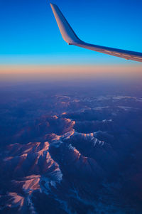 Aerial view of the plane's wing and the snow-capped mountains outside from the plane's window