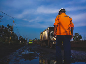 Rear view of worker standing on road against sky
