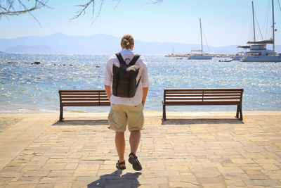 Rear view of woman standing on bench looking at sea