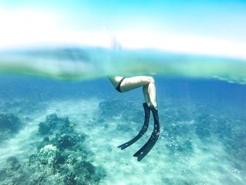 Close-up of legs with diving fins in sea against blue sky