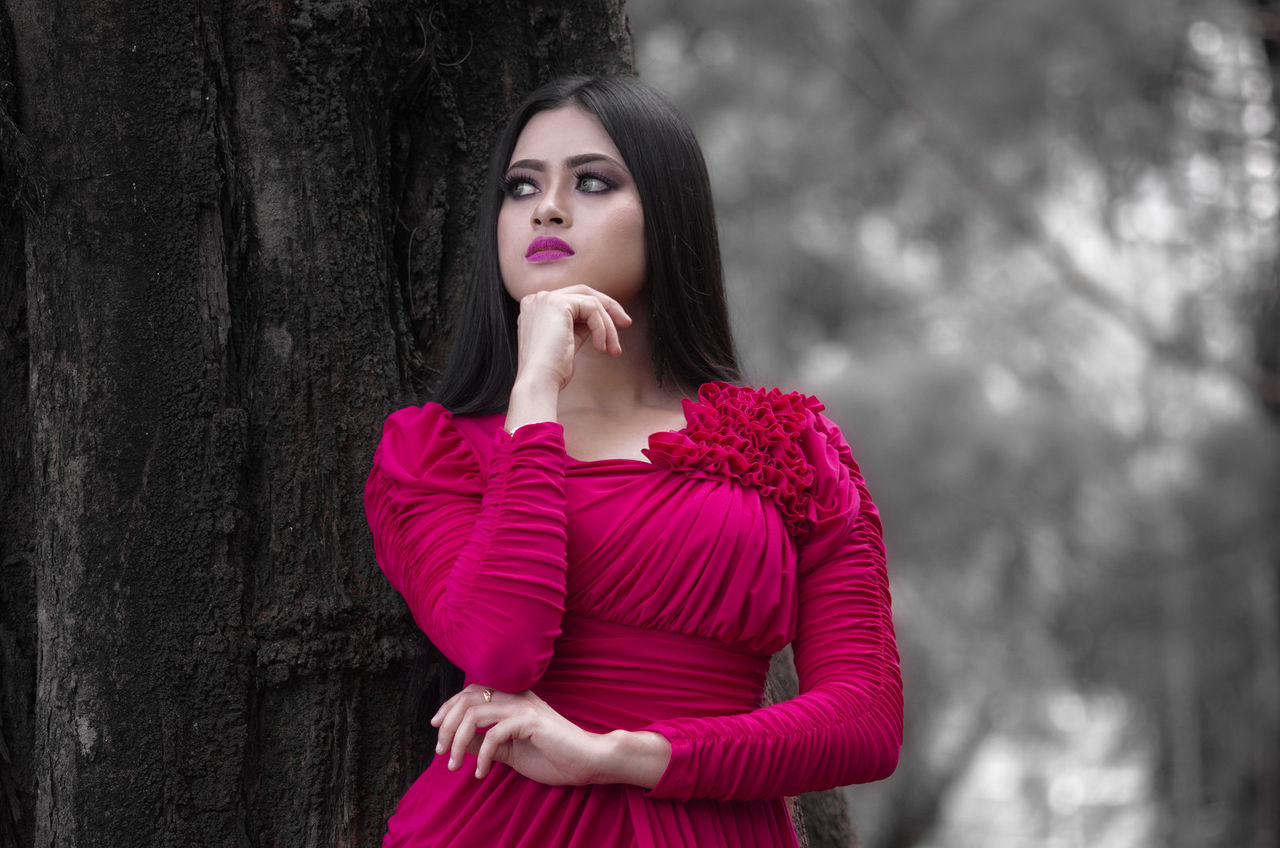 one person, young adult, standing, front view, young women, hair, beautiful woman, hairstyle, beauty, long hair, waist up, focus on foreground, women, tree, black hair, portrait, looking away, real people, casual clothing, pink color, fashion, hand, teenager, contemplation