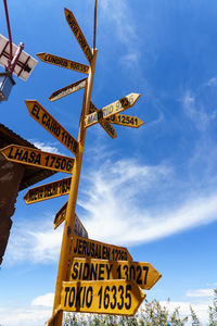 Low angle view of yellow directional sign against blue sky