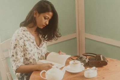 Young woman reading book on table in cafe