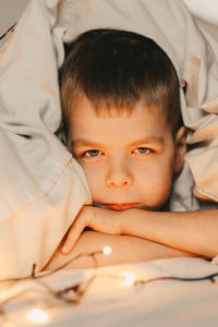 Portrait of a smiling boy lying under a white blanket and with a garland. child's christmas morning. 