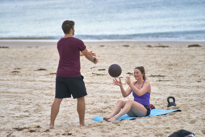 Young woman exercising with fitness instructor at beach