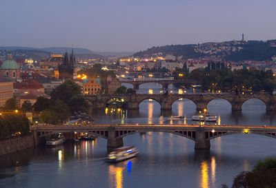 Bridge over river by illuminated buildings against sky at night