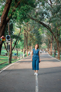 Woman walking on footpath amidst trees at park