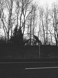 Silhouette of bare trees by road against sky