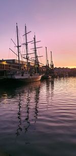 Sailboats moored in sea against sky during sunset