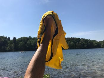 Man holding shorts by lake against sky