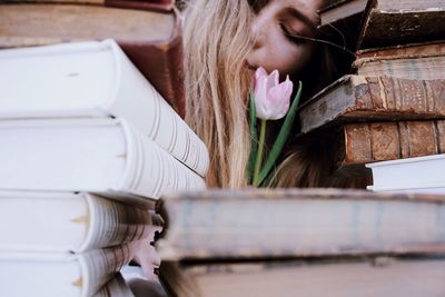 Young woman with pink flower amidst stack of books