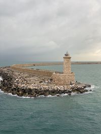 Lighthouse on sea by building against sky